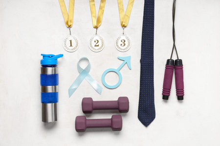 Tie, dumbbells, water bottle, medals, male sign and light blue ribbon on white background. Prostate cancer awarenessの写真素材
