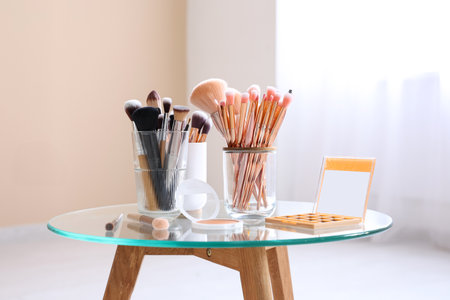 Holders with makeup brushes, palette of eyeshadows and blush on table at homeの写真素材