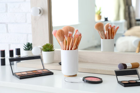 Holder with makeup brushes and different decorative cosmetics on white table at homeの写真素材