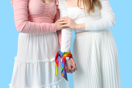 Young lesbian couple holding hands with LGBT flag on blue backgroundの写真素材
