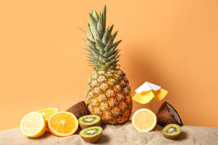 Fresh pineapple with orange, lemon, kiwi and coconut on sand against color backgroundの写真素材