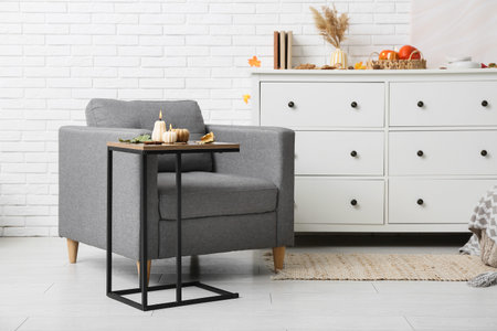 Stylish living room interior with burning candles in shape of pumpkins and autumn leaves on coffee...