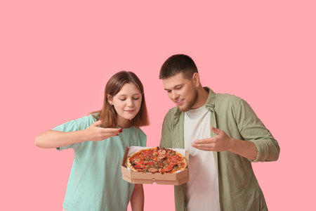 Beautiful young happy couple with cardboard box of tasty pizza on pink backgroundの写真素材