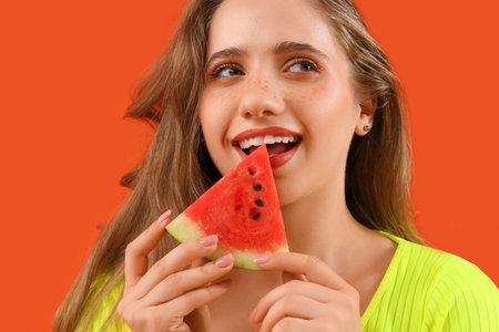 Beautiful young happy woman with piece of fresh watermelon on orange backgroundの写真素材