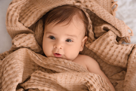 Cute little baby with beige plaid lying on bed, closeup
