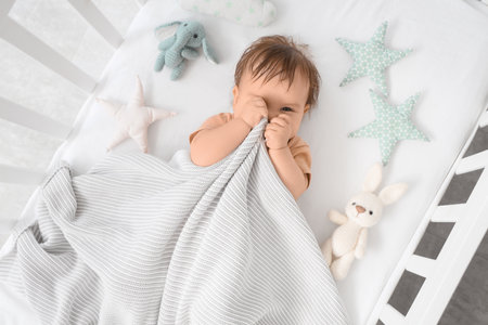 Cute little baby with plaid and toys lying in crib, top viewの写真素材