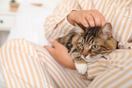 Beautiful mature woman in pajamas with cute cat sitting on bed at home, closeupの写真素材