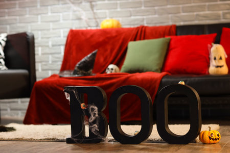 Interior of festive living room with sofa, word BOO and Halloween decorations in evening