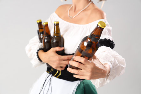 Beautiful mature Octoberfest waitress with bottles of beer on gray background, closeupの写真素材