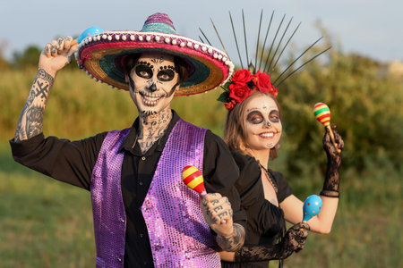 Young happy couple dressed for Mexico's Day of the Dead (El Dia de Muertos) with maracas in park...