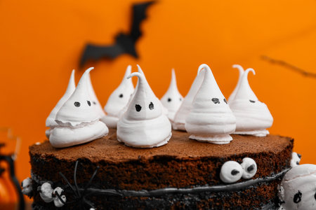 Tasty Halloween cake with ghosts and eyes on black table against orange backgroundの写真素材
