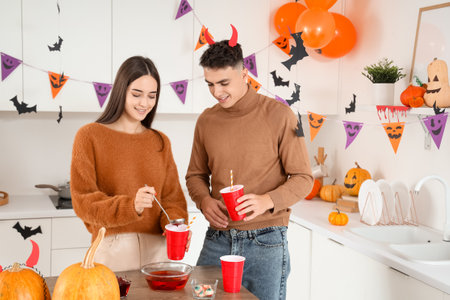 Young happy couple pouring punch into cups in kitchen decorated for Halloween partyの写真素材