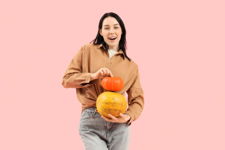 Beautiful young happy woman with pumpkins on pink backgroundの写真素材