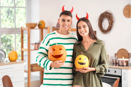 Young happy couple with Jack-O-Lantern pumpkins in kitchen decorated for Halloween partyの写真素材