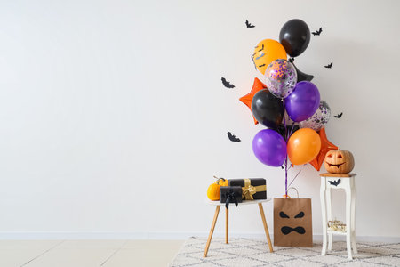 Colorful Halloween balloons with pumpkins and gift boxes near white wallの写真素材