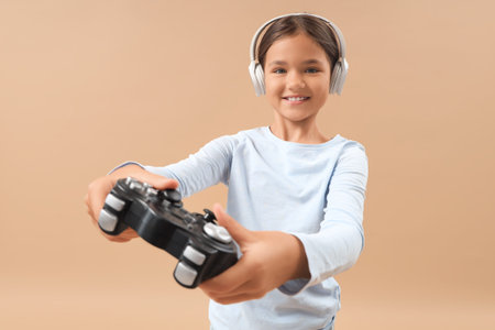 Little girl in headphones playing video game on beige background