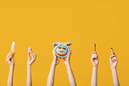Women holding funny pumpkin with facial mask, headband and decorative cosmetics on yellow backgroundの写真素材