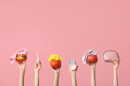 Women holding funny pumpkins with facial masks, cosmetics and bag on pink backgroundの写真素材