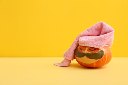 Funny pumpkin with cosmetic mask, under-eye patches and towel on color backgroundの写真素材