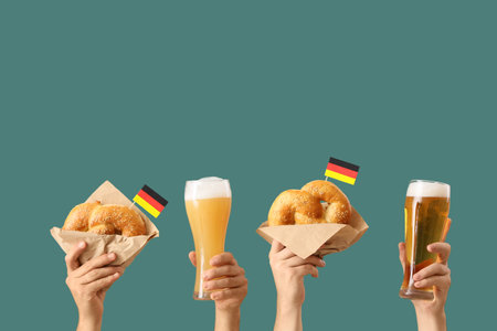Male hands with glasses of cold beer, Germany flags and traditional pretzels on green background. Octoberfest celebrationの写真素材