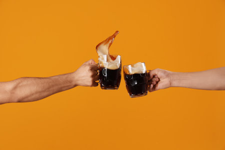 Male hands with glasses of cold beer clinking on orange background. Octoberfest celebrationの写真素材