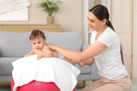 Happy mother massaging her little baby on fitball at homeの写真素材