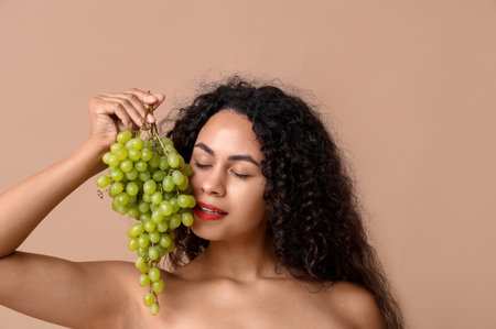 Pretty young African-American woman with sweet ripe grapes on brown backgroundの写真素材
