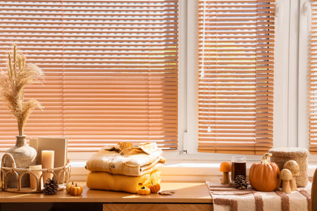 Stack of stylish clothes with autumn decorations on commode near window in living roomの写真素材