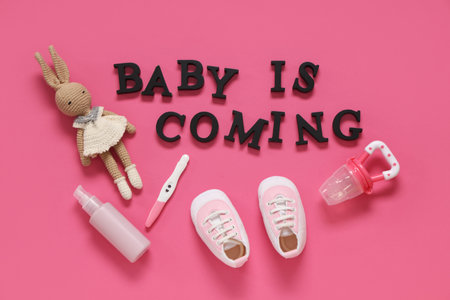 Composition with shoes, bottles, pregnancy test and text BABY IS COMING on pink background