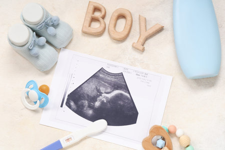 Composition with baby shoes, sonogram image, pregnancy test and word BOY on grunge beige background