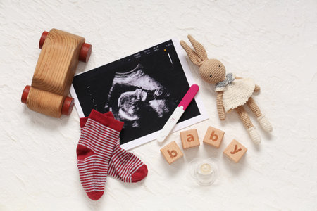 Composition with baby socks, sonogram image, pregnancy test and word BABY on grunge white background