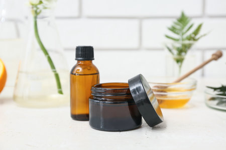 Laboratory glassware with ingredients and samples for preparing natural cosmetics on white table near brick wallの写真素材