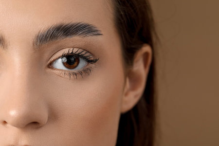 Young woman with beautiful eyebrows on brown background, closeupの写真素材