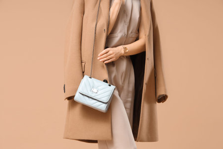 Beautiful young woman with stylish blue bag on beige background, closeupの写真素材