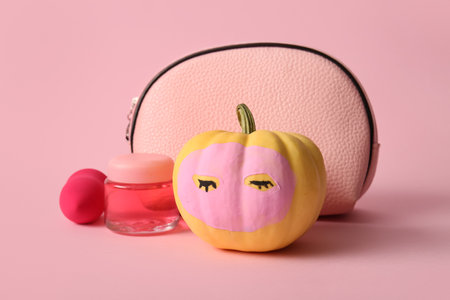 Funny pumpkin with facial mask, jar of cosmetic product and bag on pink backgroundの写真素材