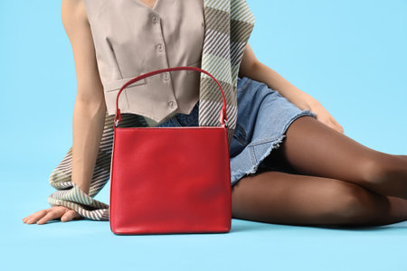 Beautiful young woman with stylish red bag sitting on blue background, closeupの写真素材