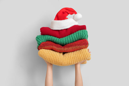 Woman holding stack of winter clothes with Santa hat near white wallの写真素材