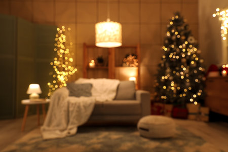 Blurred view of living room with sofa, Christmas tree and glowing lamps at nightの写真素材