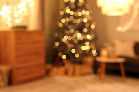 Blurred view of living room with sofa, commode and glowing Christmas tree at nightの写真素材