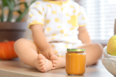 Cute little baby with jar of tasty food sitting in kitchen at home, closeupの写真素材