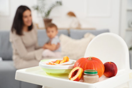 Mother with cute little baby, bowl of tasty food and fruits on table sitting at homeの写真素材