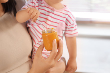Mother with cute little baby and jar of tasty food in kitchen at home, closeupの写真素材
