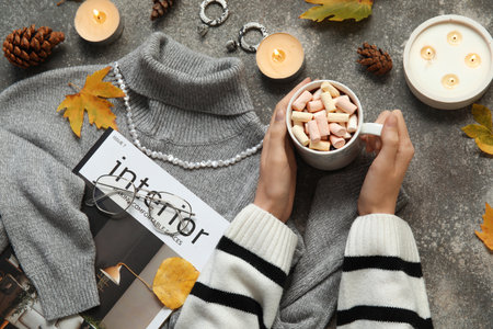 Female hands with cup of cocoa with marshmallow, sweater and accessories on gray grunge backgroundの写真素材