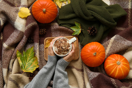 Female hands with cup of cocoa, sweater and pumpkins on plaid as backgroundの写真素材