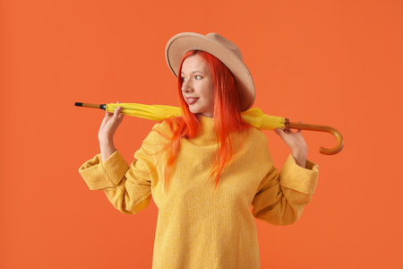 Beautiful young happy woman in autumn outfit with umbrella on orange backgroundの写真素材