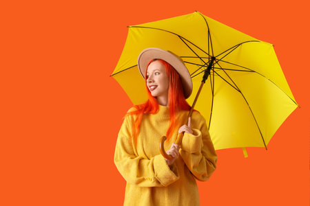 Beautiful young happy woman in autumn outfit with umbrella on orange background