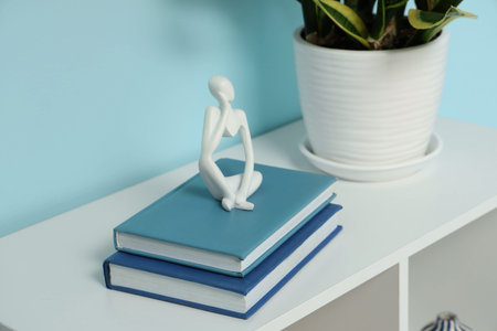 Stack of books and decorative figurine on shelving unit near blue wall