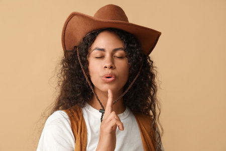 Beautiful African-American cowgirl showing finger gun gesture on beige backgroundの写真素材