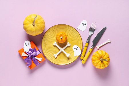 Festive table setting for Halloween celebration with gift box, pumpkins and paper ghosts on purple backgroundの写真素材