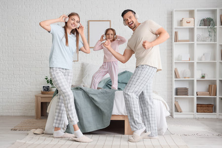 Cute little girl and her parents with headphones dancing in bedroomの写真素材